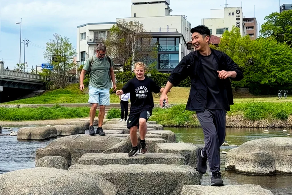 Guests crossing the Kamo River stepping stones during the SunnyCycle Kyoto e-bike tour